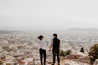 man and woman holding their hands together while standing on top of cliff