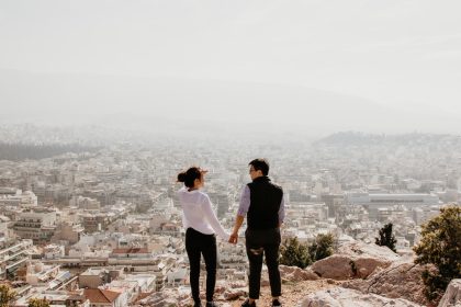 man and woman holding their hands together while standing on top of cliff