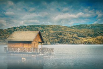 brown wooden floating cottage in middle of body of water with mountain in background