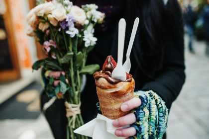 Woman holding a chocolate pastry and bouquet, capturing a street food moment.