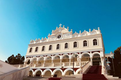 a large white building with red stairs with Tinos in the background