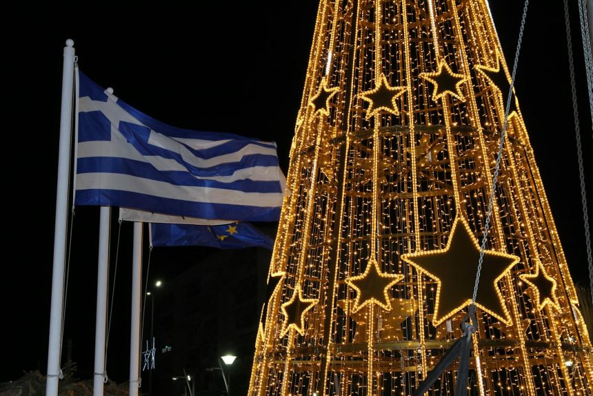 A glowing Christmas tree with Greek flags waving at night, creating a festive atmosphere.