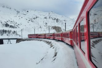 a red train traveling down train tracks next to a snow covered mountain